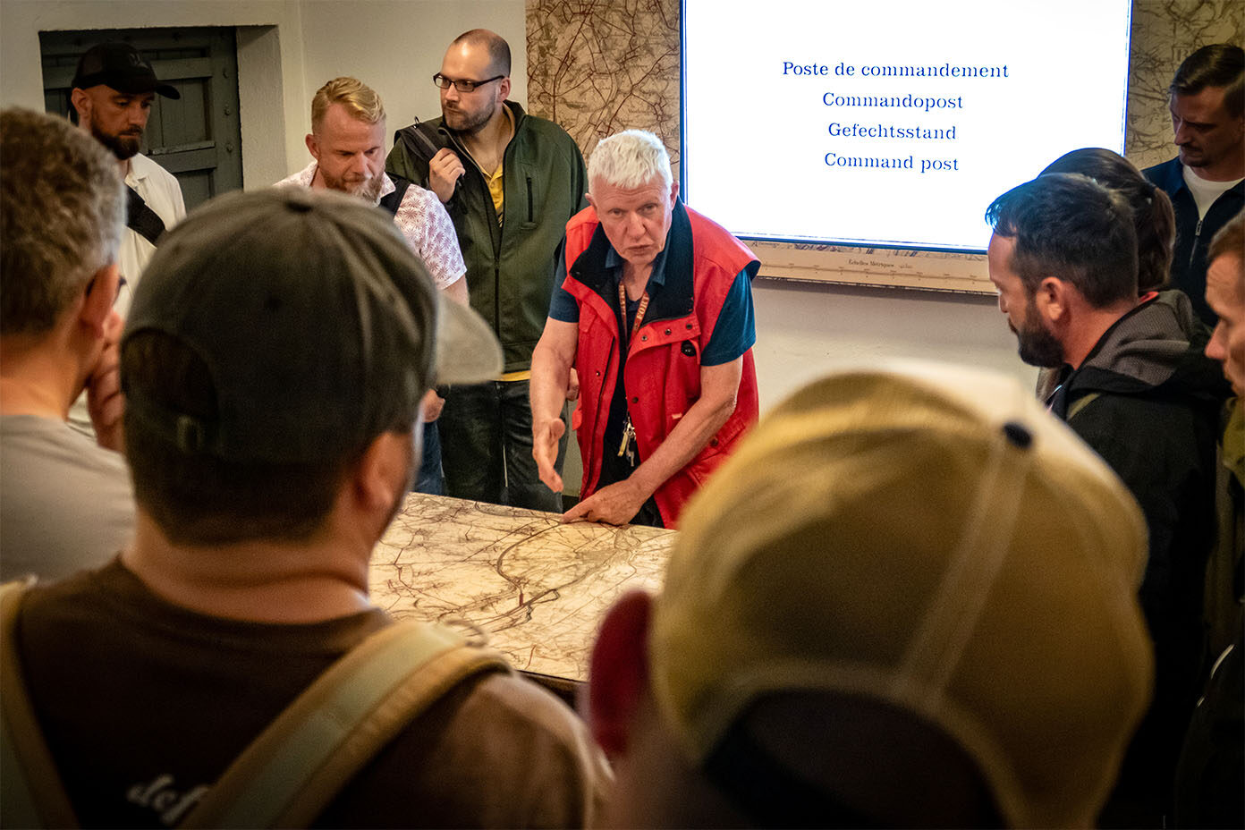 Gruppe von Menschen steht um einen Tisch mit einer großen Karte, während eine Person in roter Weste spricht.