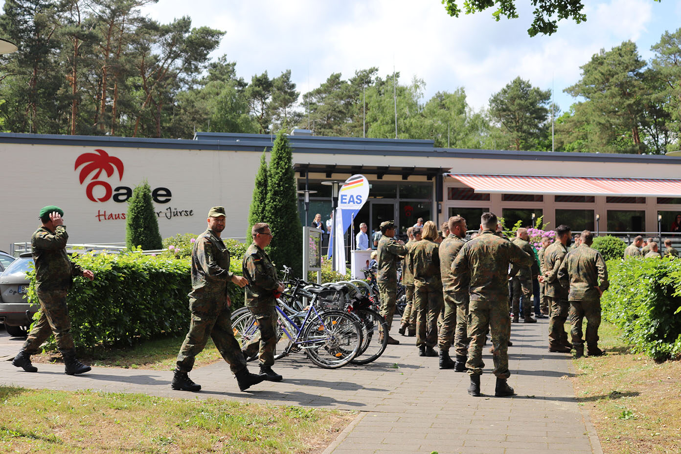 Gruppe von Soldaten in Uniformen steht und geht vor einem Gebäude mit dem Schriftzug "Oase - Haus an der Jürse".