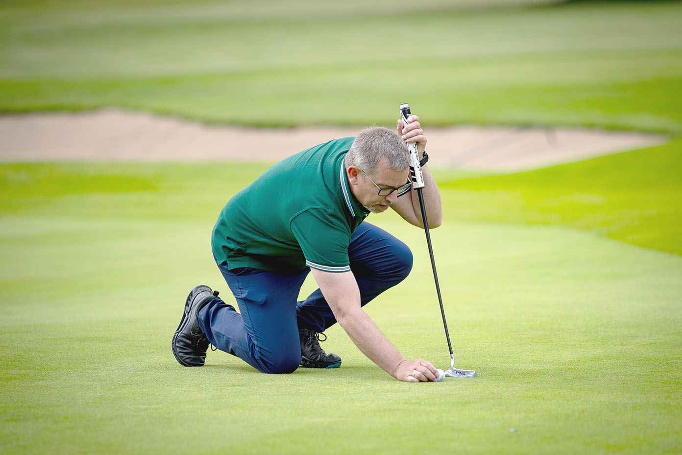 Eine Person kniet auf einem Golfplatz und legt einen Golfball auf das Grün, während sie einen Golfschläger hält.