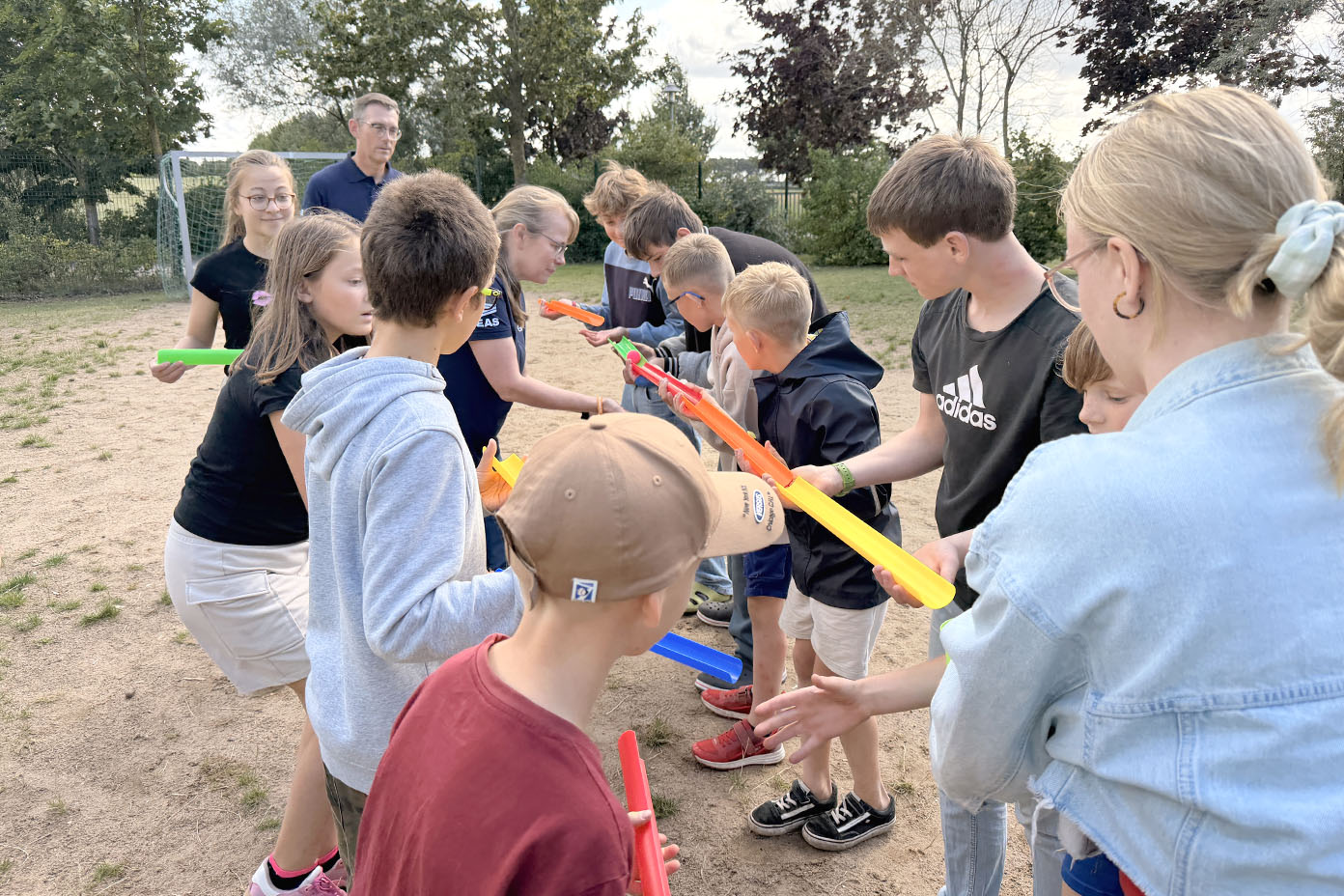 Eine Gruppe von Kindern und Erwachsenen steht im Freien auf einem Spielfeld und spielt mit bunten Wasserrinnen.
