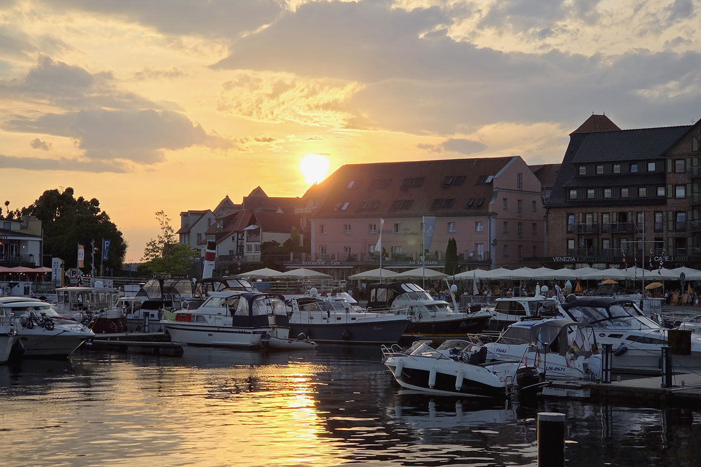 Boote liegen im Hafen bei Sonnenuntergang vor einer Reihe von Gebäuden mit Cafés und Restaurants.