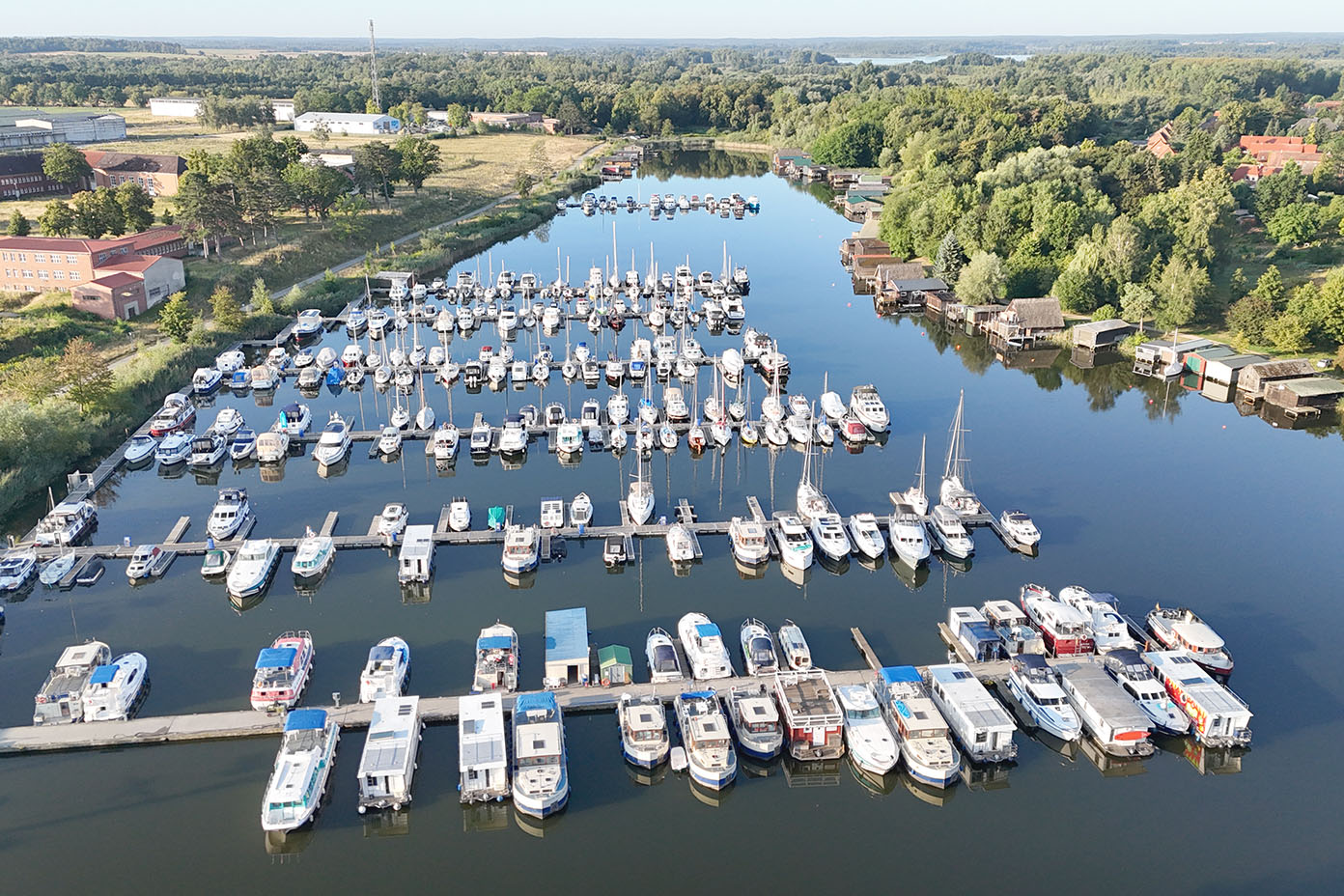Ein ruhiger Hafen mit zahlreichen festgemachten Booten und umgeben von grünen Bäumen und Gebäuden im Hintergrund.