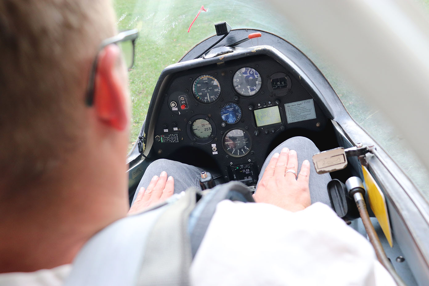 Eine Person sitzt in einem Cockpit eines Segelflugzeugs und blickt auf das Instrumentenbrett mit verschiedenen Anzeigen und Messgeräten.