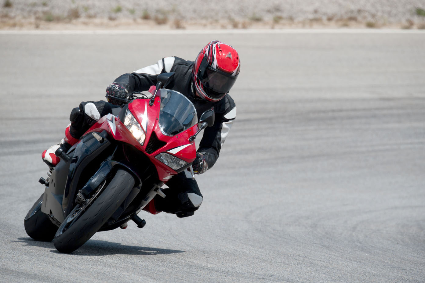 Eine Person in schwarzer Schutzkleidung und rotem Helm fährt mit einem roten Motorrad auf einer kurvigen Rennstrecke.