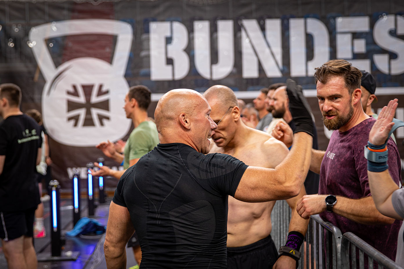 Mehrere Personen in Sportkleidung stehen in einer Halle vor einem Banner mit der Aufschrift „BUNDESWEHR-THROWDOWN“ und unterhalten sich, wobei eine Person die Faust hebt.